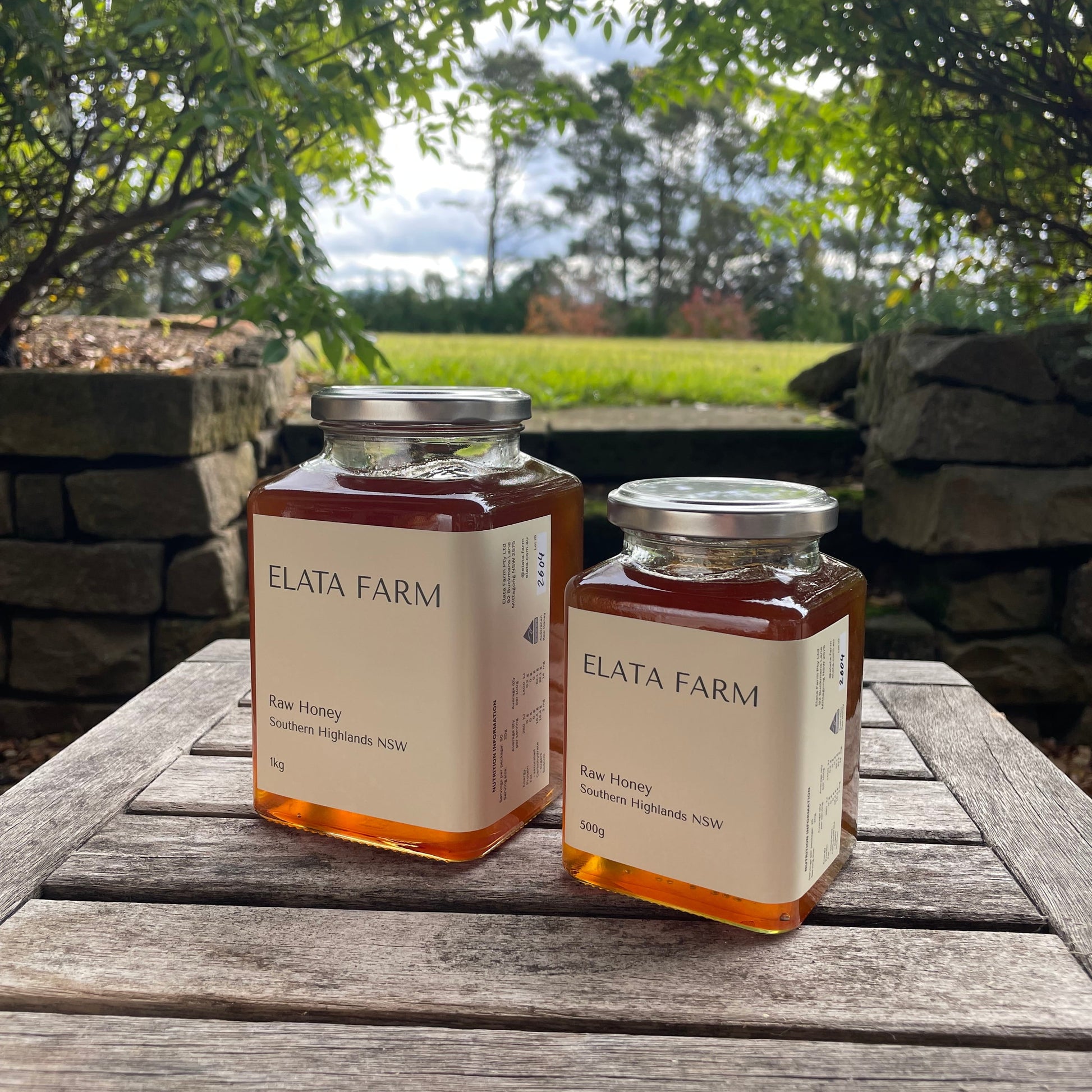 Two jars of Elata Farm honey on a wooden table with a natural outdoor background.